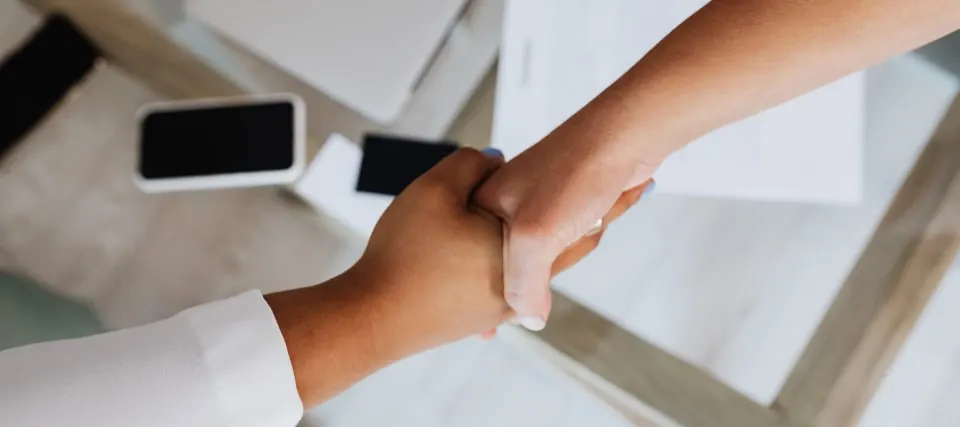 Two people shaking hands across a desk