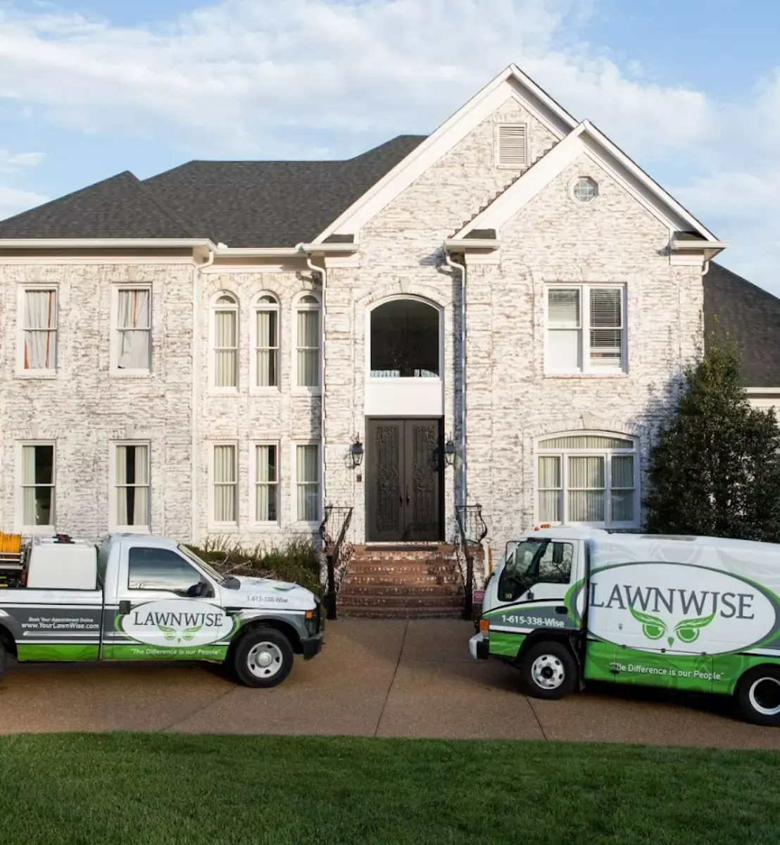 Two green LawnWise trucks parked outside a stone home